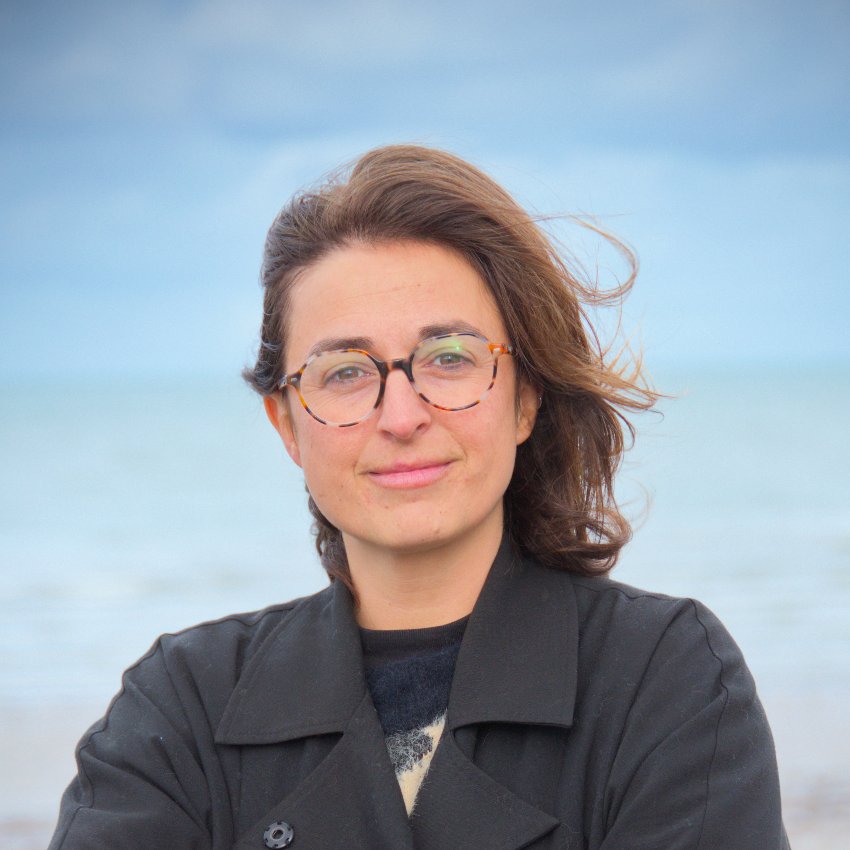 portrait de Domitille Nicolet qui sourit, elle porte des lunettes, elle est devant la mer