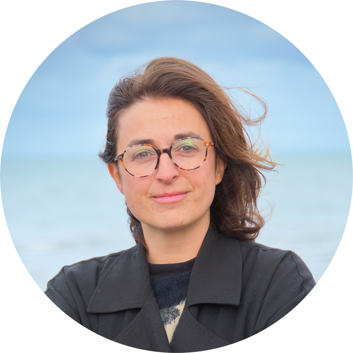 portrait de Domitille Nicolet qui sourit, elle porte des lunettes, elle est devant la mer